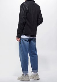 Černá kožená bunda s přiléhavým střihem, s vysokým límcem a stříbrným zipem. Kombinována s volnými modrými džínami a světlými teniskami.