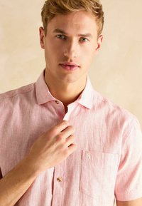 Lühikeste varrukatega, heledad roosa nuppude särgid, millel on vertikaalne triibuline muster, üks rinna tasku ja beežid nööbid.