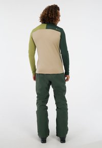 Langarmtop in beige, groen en donkergroen kleurvlak ontwerp; gecombineerd met donkergroene taps toelopende broek. Glad fabric, atletische pasvorm.