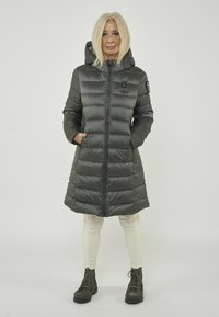 Daunenjacke in Dunkelgrau, mit Reißverschluss vorne, Kapuze und gestepptem Design. Seitliche Taschen, kombiniert mit cremefarbenen Hosen und Stiefeln.