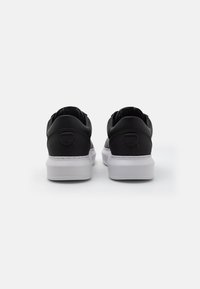 Black leather sneakers with a white rubber sole, featuring a smooth texture, rounded shape, and a subtle logo on the back.