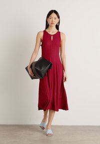 Burgundin ilmanhihaista mekkoa, jossa on aukko yksityiskohtana ja liehuva helma, on yhdistetty mustaan laukkuun ja vaaleansinisiin liukuvaatteisiin. Sujuva rakenne.