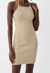Robe en tricot côtelé beige avec une silhouette ajustée, un design à col halter et une texture côtelée, s'étendant jusqu'à mi-cuisse.