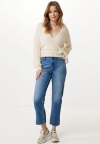 Cremfarbener, flauschiger Wickelpullover mit langen Ärmeln und Bindedetail, kombiniert mit hellblauen, geraden Jeans und beige Sneakers. Minimalistisches Design.