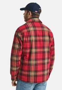 Rot-schwarz karierte Flanellhemd mit Kragen, langen Ärmeln und Knopfmanschetten. Über einer blauen Jeans getragen, von hinten gezeigt.