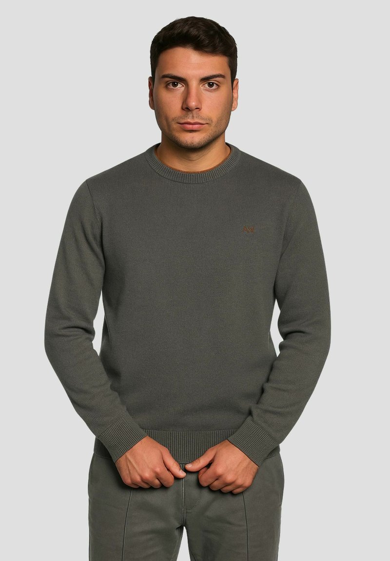 Grauer Strickpullover mit rundem Ausschnitt, gerippten Bündchen und Saum, mit einem kleinen, bestickten Logo auf der Brust, getragen mit passenden Hosen.
