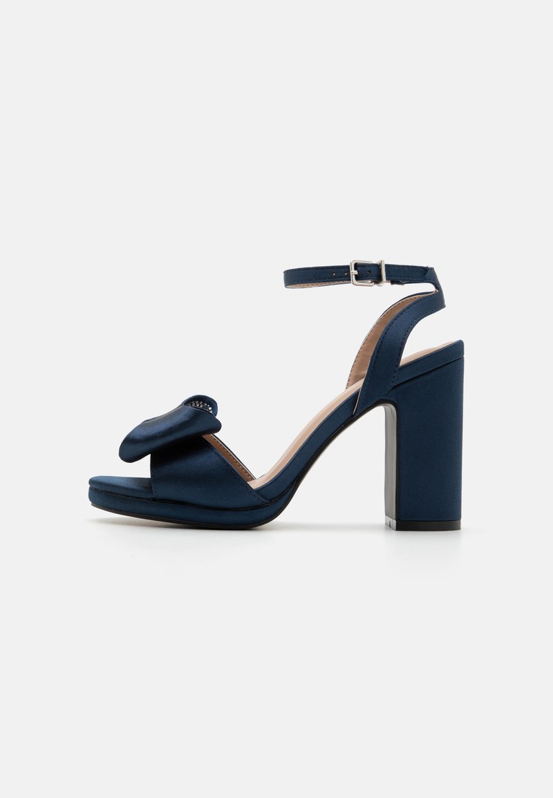 Ναυτικό μπλε σατέν σανδάλι με φαρδύ λουρί και λεπτομέρεια σε φιόγκο, ανοιχτή μύτη, λουρί στον αστράγαλο με αγκράφα και χοντρό τακούνι.
