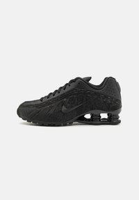 Sapatos esportivos pretos com um cabedal texturizado, perfurações e duas molas em espiral distintas no calcanhar para suporte de amortecimento.