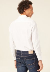 Witte langwaardige shirt met een button-down kraag, gecombineerd met donkerblauwe denim jeans met een tan leren logo label en zichtbare stiksels.