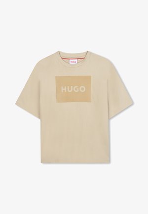 T-shirt en coton beige à manches courtes, avec un graphique rectangulaire central portant "HUGO" en blanc et des accents rayés verticaux en jaune.