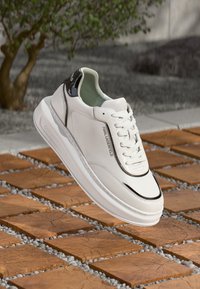 Λευκά δερμάτινα αθλητικά παπούτσια με μαύρες λεπτομέρειες, στρογγυλή μύτη και κλείσιμο με κορδόνια, με λογότυπο στο πλάι και υφασμένη σόλα.