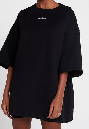 Persoon draagt een oversized zwart G-Star Raw T-shirt met korte mouwen, staand tegen een effen achtergrond.