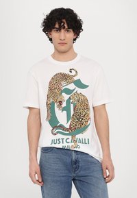 Biała bawełniana koszulka z kolorową grafiką lamparta i zielonym napisem "JUST CAVALLI MILANO". Krótkie rękawy i luźny krój.
