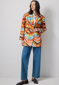 Colorful blazer with wavy patterns in orange, blue, yellow, and brown. Features a single button closure and two front pockets. Paired with wide-leg jeans.