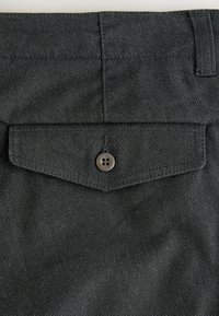 Dark gray fabric pants with a textured weave, featuring a back pocket and a brown button closure. Decorative stitching is visible.
