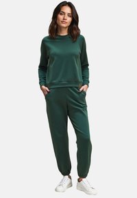 Groene sweatshirt en bijpassende joggers van zachte stof, met een relaxte pasvorm, elastische manchetten en zijzakken. Witte sneakers maken de look af.