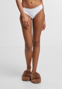 White cotton bikini underwear with lace trim, paired with brown fuzzy slippers. The fabric appears soft with a smooth texture.
