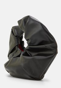 Zwarte leren tas met een unieke gedraaide vorm, voorzien van zachte plooien en een gladde textuur. Interieur gevoerd in het rood, wat het contrast versterkt.