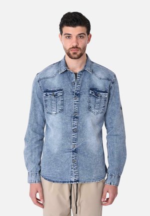 Camicia in denim blu chiaro con maniche lunghe, chiusura frontale con bottoni, due tasche sul petto e cuciture a contrasto lungo le cuciture.
