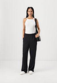 Valge ribadega spagetti рестапiga tank top, millele on sobitatud laiad mustad elastse vöökoha püksid ja valged tennisetossud. Lihtne käekott.