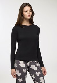 Czarna bluzka z długim rękawem wykonana z gładkiego materiału, z okrągłym dekoltem. W zestawie z szarymi spodniami od piżamy zdobionymi białymi nadrukami misiów.