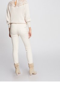 Suéter de canalé crema con detalle de encaje en la parte trasera, combinado con pantalones ajustados crema y botas de ante beige hasta el tobillo con puños doblados.