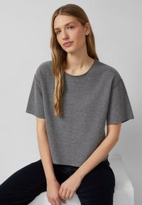 Graues T-Shirt mit kurzen Ärmeln und rundem Halsausschnitt, aus strukturiertem Strickstoff mit lockerem Schnitt, kombiniert mit dunklen Hosen.