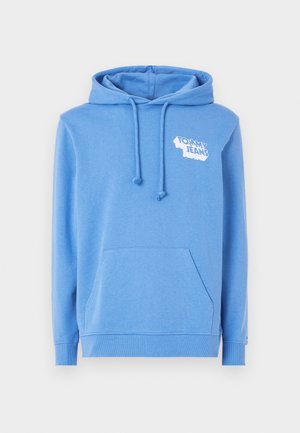 Sininen puuvillapaita, jossa on kengurutasku, naruhuppu ja valkoinen logo "TOMMY JEANS" vasemmalla yläpuolella. Pehmeä rakenne, rento muotoilu.