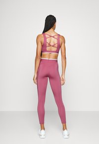 Completo da allenamento aderente in mauve, composto da un reggiseno sportivo a spaghetto con design della schiena incrociato e leggings a vita alta. Texture liscia.