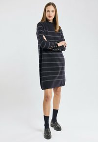 Robe rayée navy à manches longues, col haut et accents de boutons aux poignets. Présente une coupe décontractée et un tissu doux et texturé.