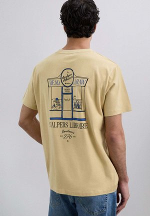 Camiseta de algodón amarilla con un diseño gráfico azul en la parte de atrás, que representa una librería con el texto "LEER" y "DIBUJAR". Mangas cortas.