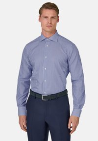 Camisa de vestir a rayas azules y blancas con mangas largas, tapeta de botones y puños en contraste, combinada con pantalones oscuros azules y un cinturón verde.