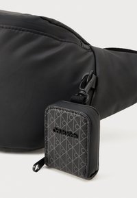 Fekete szövet válltáska sima felülettel, levehető, geometrikus mintákkal díszített kisebb tasakkal és Calvin Klein logóval.