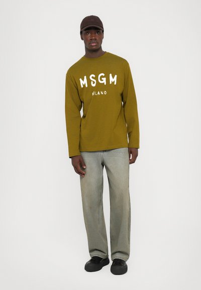 Oliivroheline pika varrukaga särk valge "MSGM MILANO" tekstiga, helehallad teksased ja mustad kingad. Lihtne, keha järgi lõigatud disain ümarate kaelustega.
