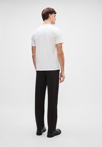 T-shirt branco de manga curta combinado com calças largas e escuras. O conjunto apresenta um design limpo e simples, com um ajuste casual.