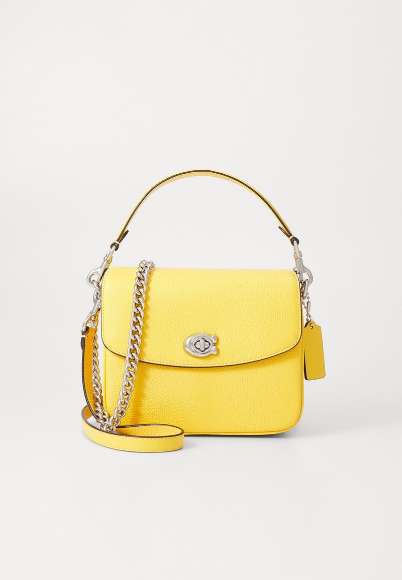 Sac à main en cuir jaune avec fermoir tourniquet argenté, poignée supérieure et bandoulière chaîne argentée, sur fond blanc uni.