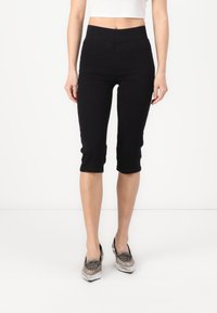 Svarte capri-bukser med høy midje, laget av stretchmateriale. Har en glatt tekstur og en tettsittende silhuett, som avsluttes rett under kneet.