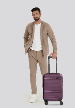 Maleta dura morada con estrías horizontales; cuenta con un mango telescópico y cuatro ruedas para facilitar el desplazamiento.