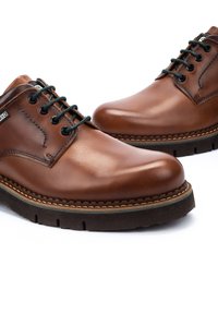 Zapatos de cuero marrón de cordones con un acabado suave, puntera redonda, cordones negros y suela de goma texturizada con detalles de costura en contraste.