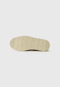 Suela de zapato con una superficie de goma beige texturizada, que presenta patrones en zigzag y surcos para mayor tracción. Diseño de punta plana y redondeada.