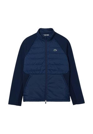 Chaqueta navy con un frente acolchado, mangas lisas, cuello alto y cierre de cremallera completo. Presenta un pequeño logo verde en el lado izquierdo del pecho.