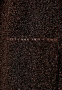 Gros plan d’un tissu texturé bouclé marron foncé avec une bande horizontale en cuir passée à travers.