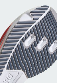 Semelle de chaussure grise avec des rainures horizontales et verticales. Comprend des découpes circulaires et des accents contrastants au talon et aux orteils.