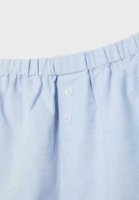 Tissu bleu clair avec taille élastique et deux boutons blancs à l'avant, probablement partie d'un short ou d'un pantalon.