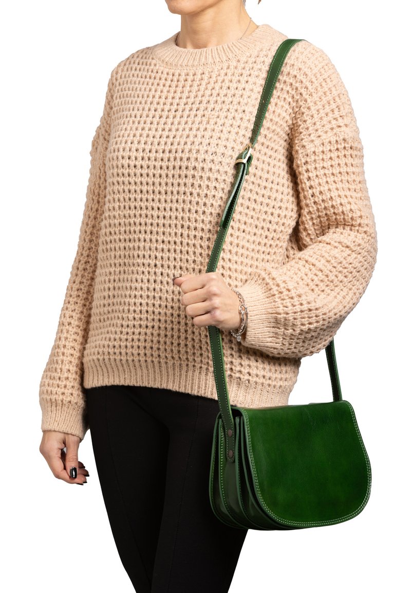 Borsa a tracolla verde in pelle con patta curvata, cuciture a contrasto e tracolla regolabile, indossata insieme a un maglione beige a trama.