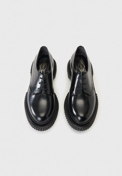 Ζευγάρι μαύρα δερμάτινα παπούτσια με κορδόνια και παχιά, ανάγλυφα πέλματα σε απλό λευκό φόντο.