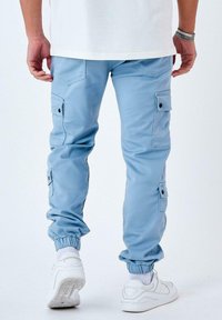 Pantalones cargo de color azul claro con puños elásticos, bolsillos laterales con solapas y textura suave. Combinados con una camisa blanca y zapatillas.