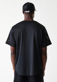Black mesh athletic shirt with short sleeves, round neckline, and perforated texture. Features a cap worn backwards with "BULLS" logo.