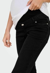 Black denim jeans with a slim fit, featuring a button closure, subtle pockets, and a smooth texture. Worn with a white top.