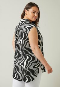Blusa a maniche corte a righe bianche e nere, con un design ondulato e un orlo posteriore più lungo. Tessuto leggero con una consistenza liscia.